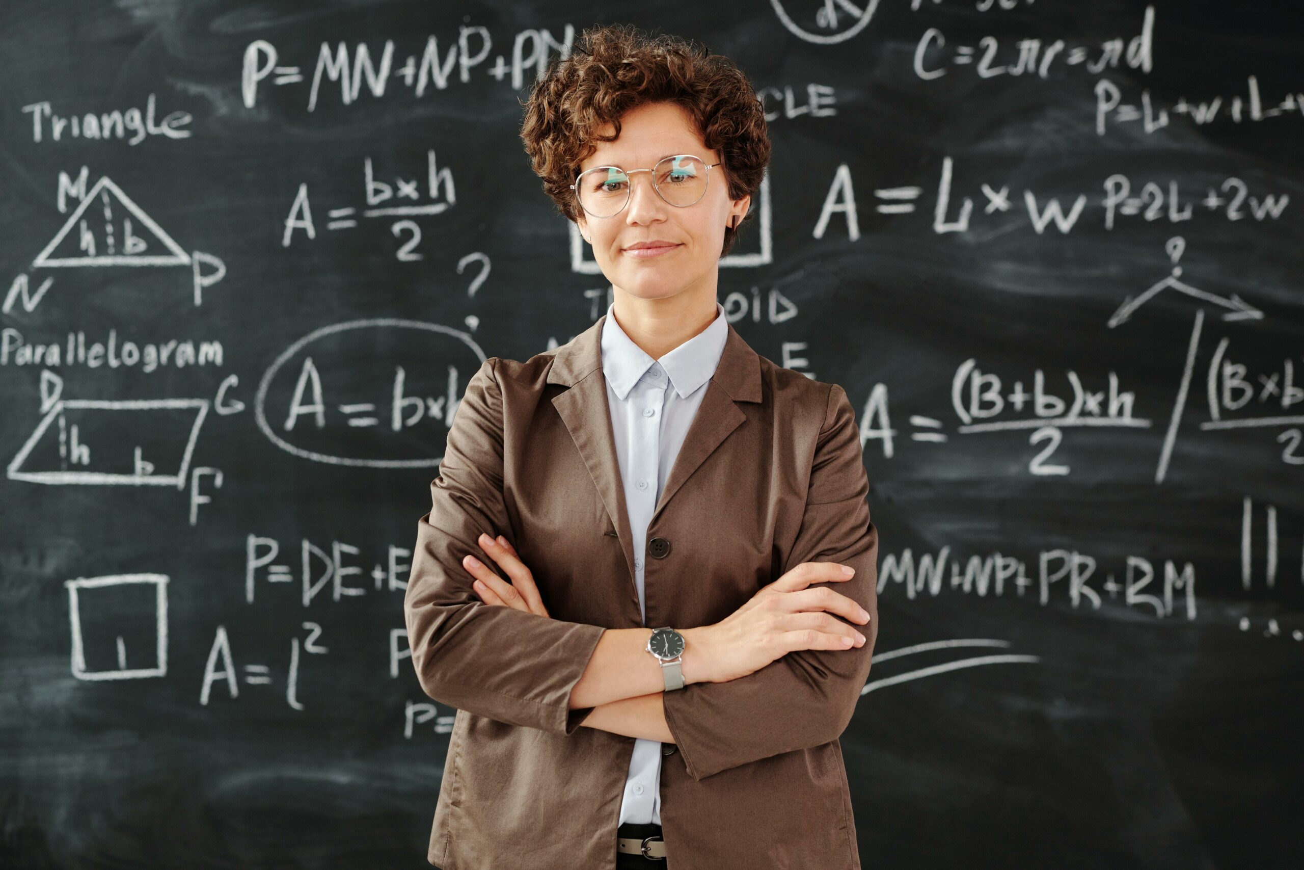 Uśmiechnięta kobieta stojąca przed tablicą pełną matematycznych wzorów, reprezentująca analityczne podejście do zarządzania kampaniami influencer marketingu.