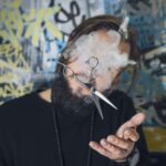 Młody mężczyzna z tatuażami i smartfonem na tle kolorowego graffiti